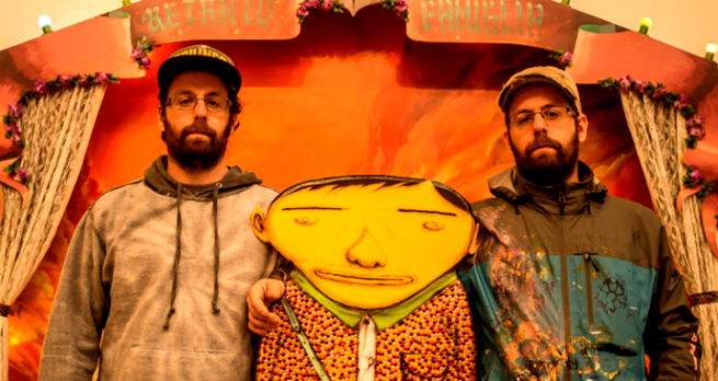 Os Gemeos abraçados com um dos seus principais personagens